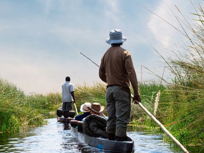 Mokorotocht door de Okavango Delta, met gids die een kano door rietvelden voortduwt.