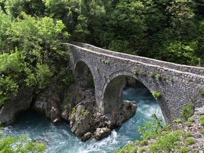 Oude stenen boogbrug over een turquoise rivier in een groene kloof op de Route Balkan.