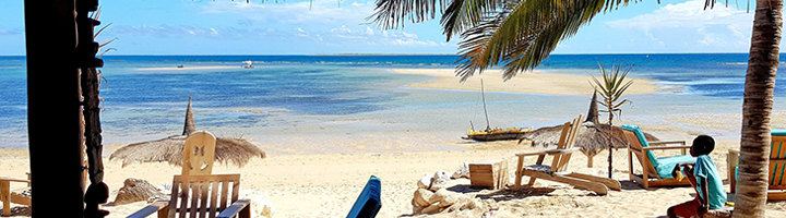 Tropisch strand met palmbomen, ligstoelen en dhow-boot op zee bij een Afrikaans eiland.