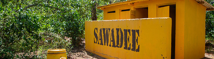 Twee gele Sawadee wc-huisjes in Oeganda, met Sawadee-logo op de muur.