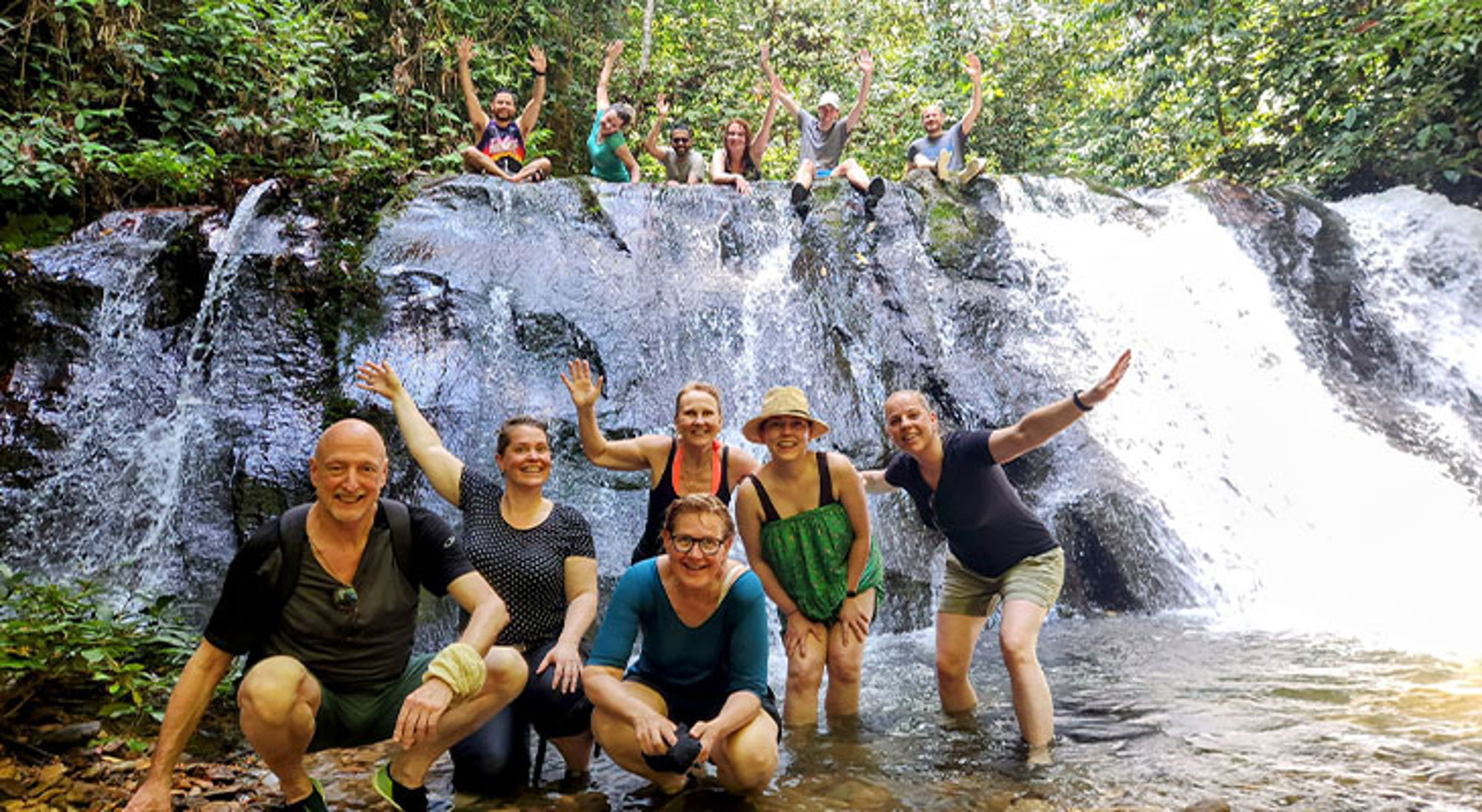 Groep reizigers poseert en zwaait bij een waterval in het regenwoud.