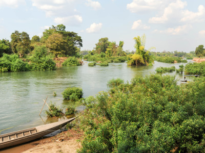 Rivierlandschap in Laos met groene oevers en een houten boot aan de waterkant.