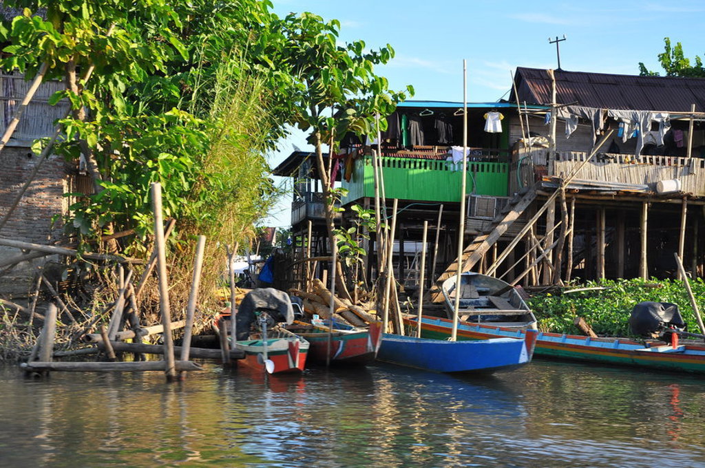 Houten paalwoningen aan de waterkant met kleurrijke bootjes in Indonesië, Kalimantan, Sulawesi en Molukken.