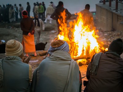 Mensen warmen zich bij een groot vuur langs de Ganges in Varanasi tijdens de Route India-reis.