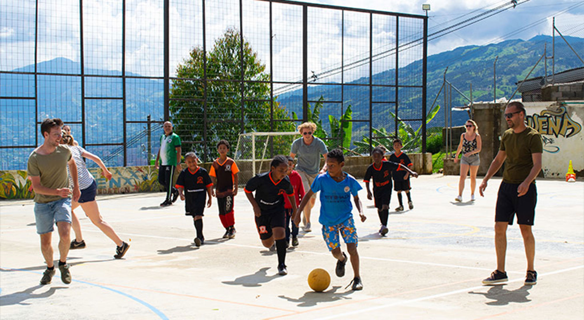 Voetballen in Medellin Kinderen en volwassenen spelen samen voetbal op een buitenveld met bergen op de achtergrond.