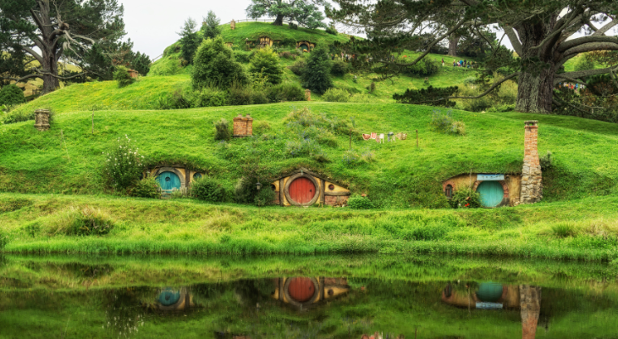 The Shire in Nieuw-Zeeland Hobbiton-hobbitwoningen met ronde deuren in groene heuvels, weerspiegeld in het water.