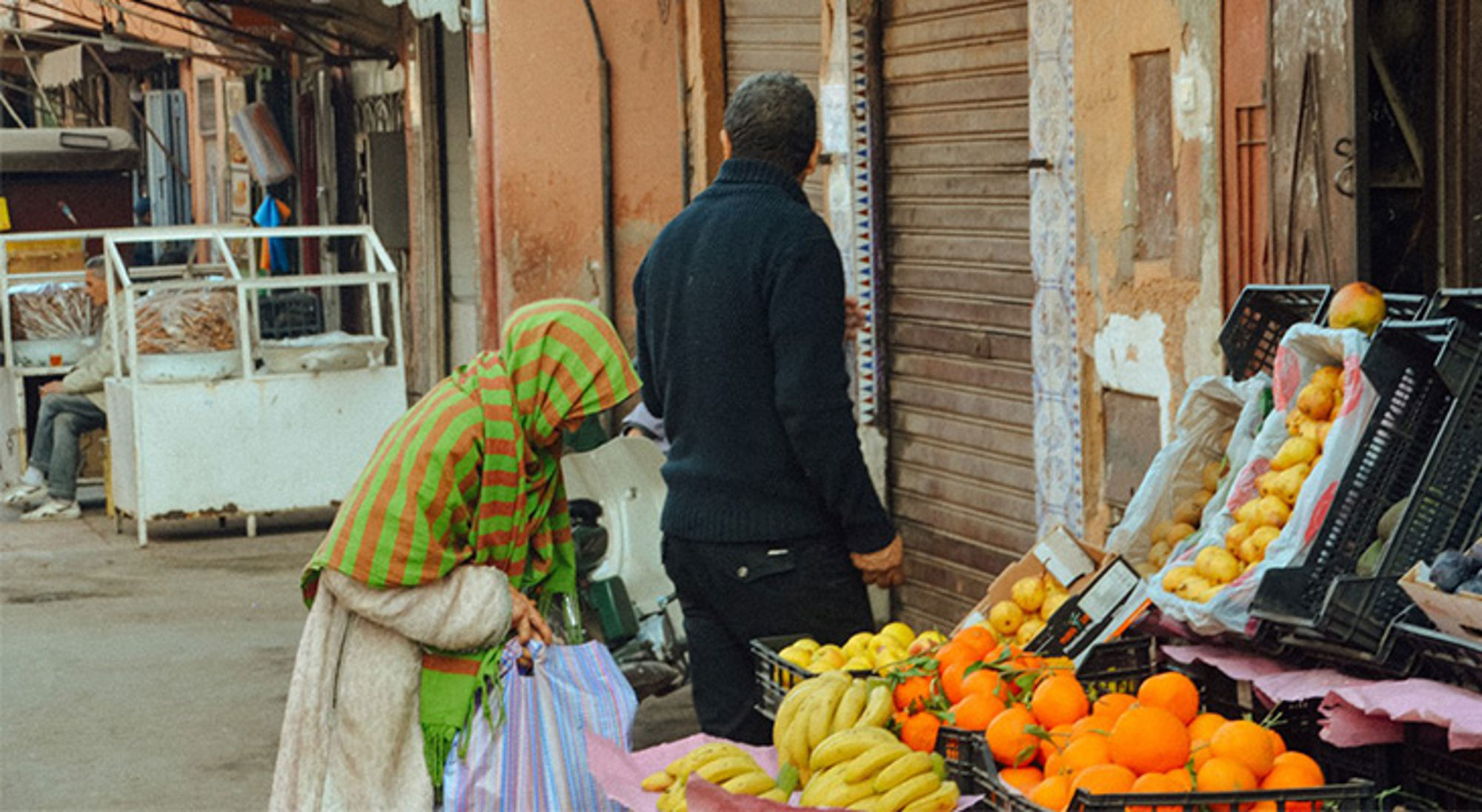 Marokkaanse markt Straatmarkt met fruitkraam vol sinaasappels en bananen, met shoppers in een smalle steeg.