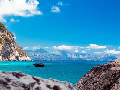 Turquoise baai met rotsachtige kust en bergen op de achtergrond tijdens wandelvakantie op Sardinië.