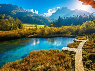 Turquoise bergmeer met houten vlonderpad, omringd door bossen en Alpenlandschap op de Route Centraal Europa.