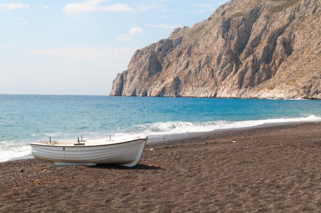 Wit bootje op zwart zandstrand met rotsachtige kustlijn op Naxos, Griekenland.