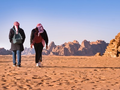 Wandelaars in de Wadi Rum-woestijn in Jordanië, met rotsformaties op de achtergrond.