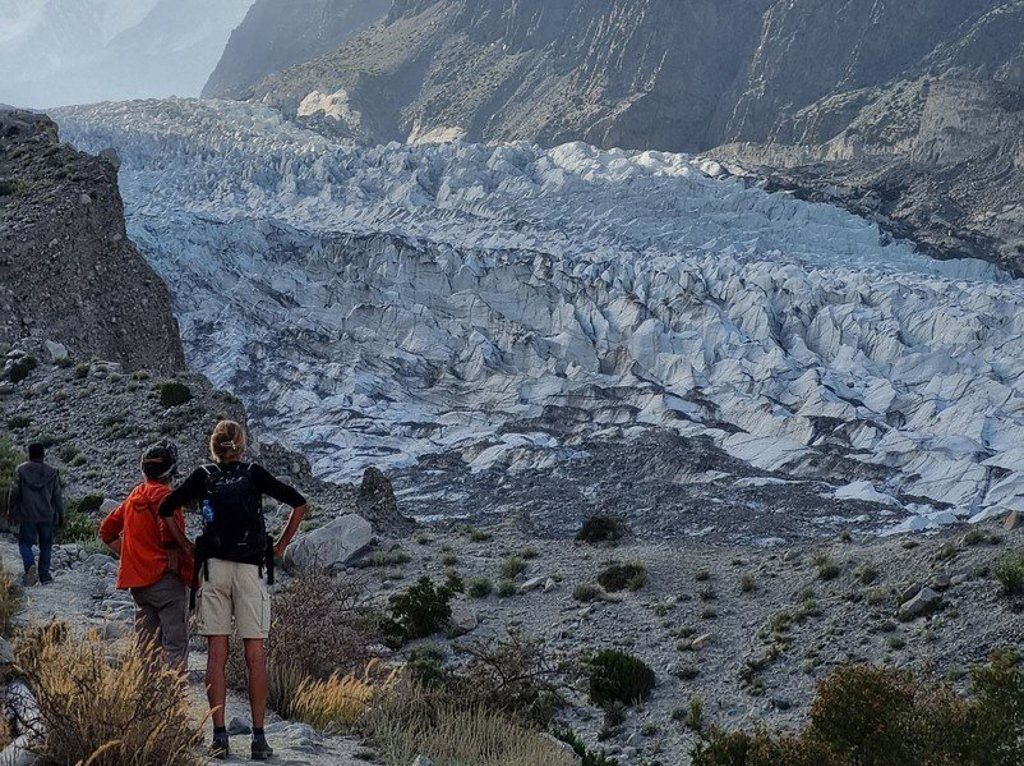 Twee reizigers wandelen door een groen berglandschap in Baltistan en Hunza, Pakistan.