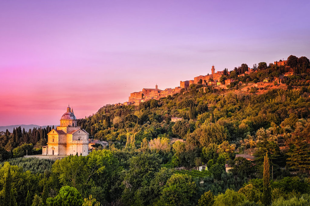 Zonsondergang over Montepulciano in Toscane met kerk en heuveldorp tussen groene wijngaarden.
