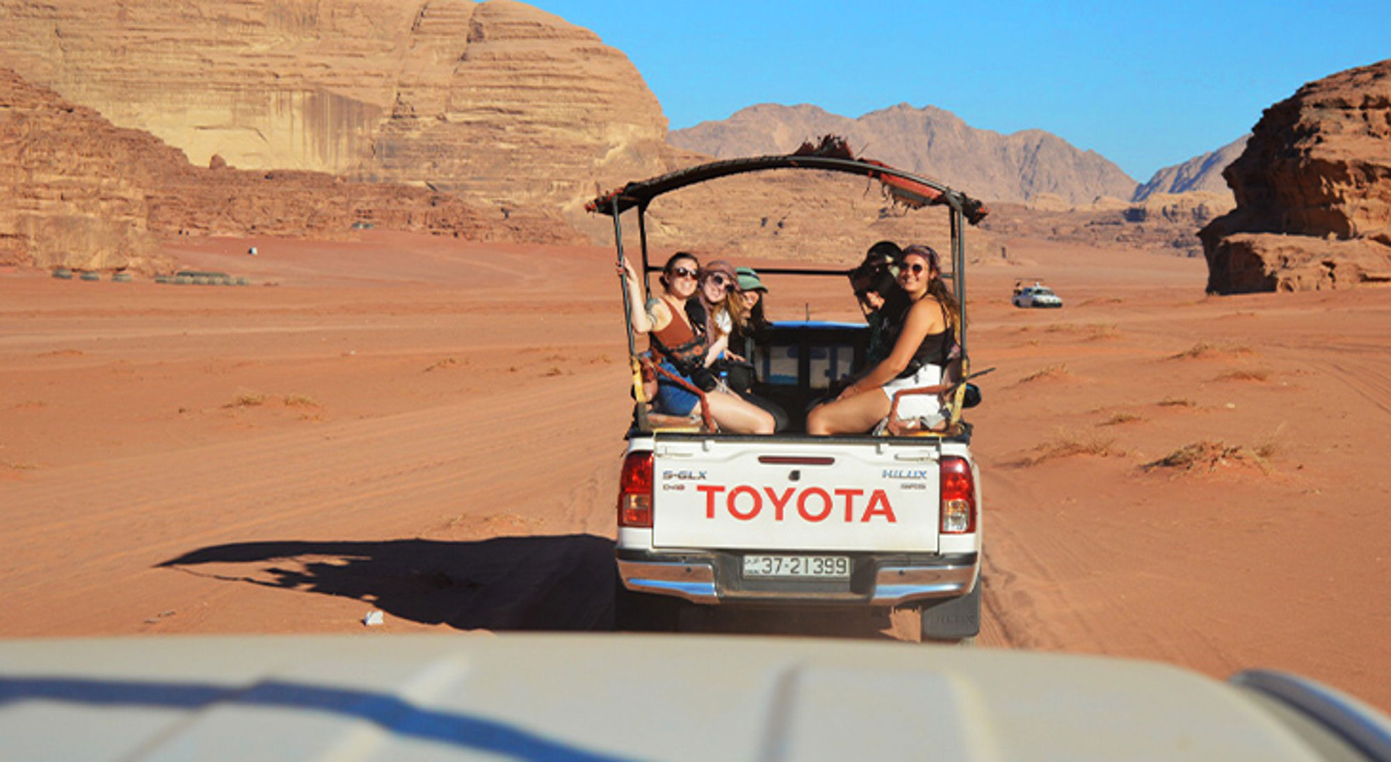 Jeep safari door de Wadi Rum-woestijn met reizigers in een pick-up en rotsformaties op de achtergrond.