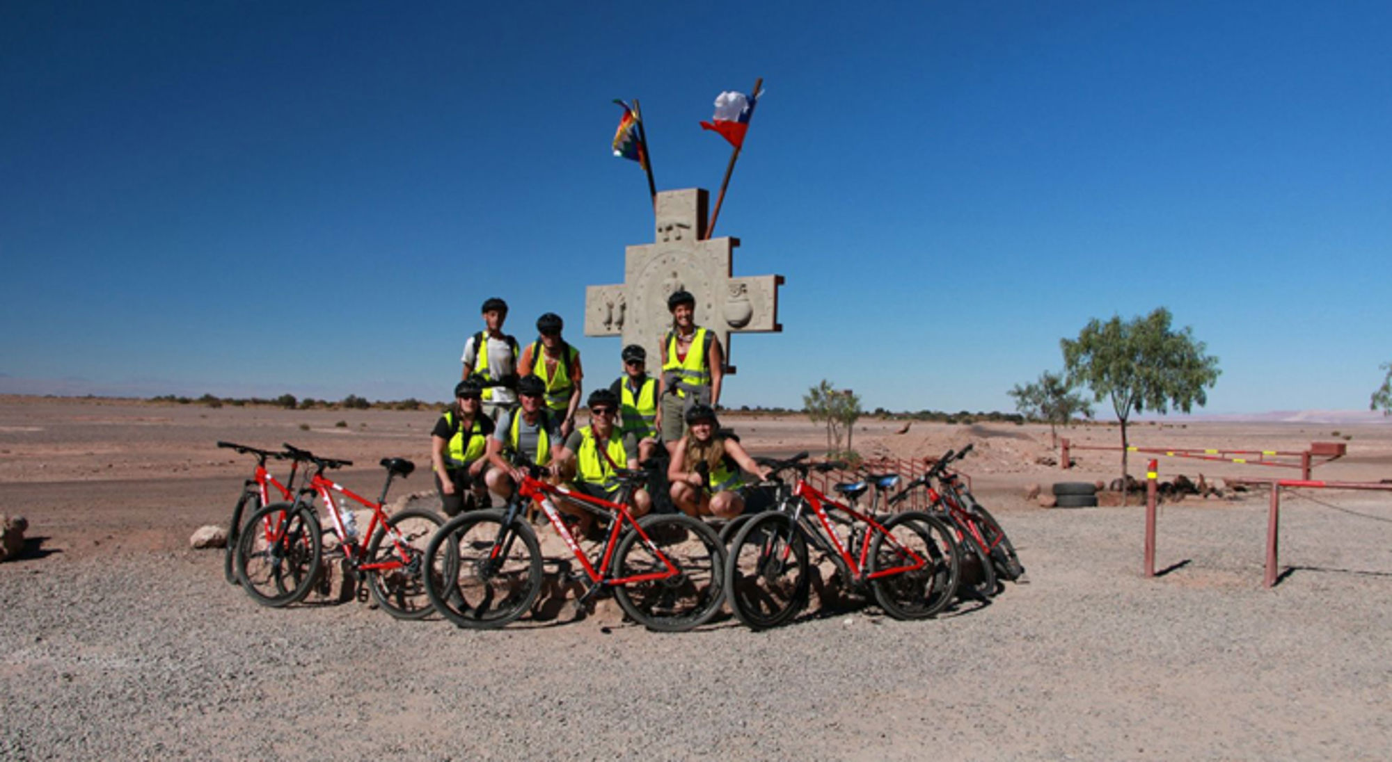 fietsen in noord-chili Groep mountainbikers poseert met fietsen bij een monument in een woestijnlandschap.