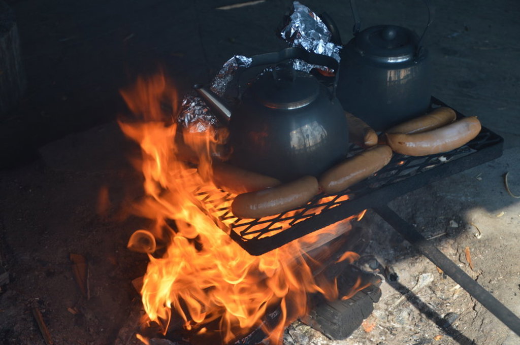 Koken boven open vuur in Lapland: koffiepotten en worstjes op een rooster bij kampvuur.