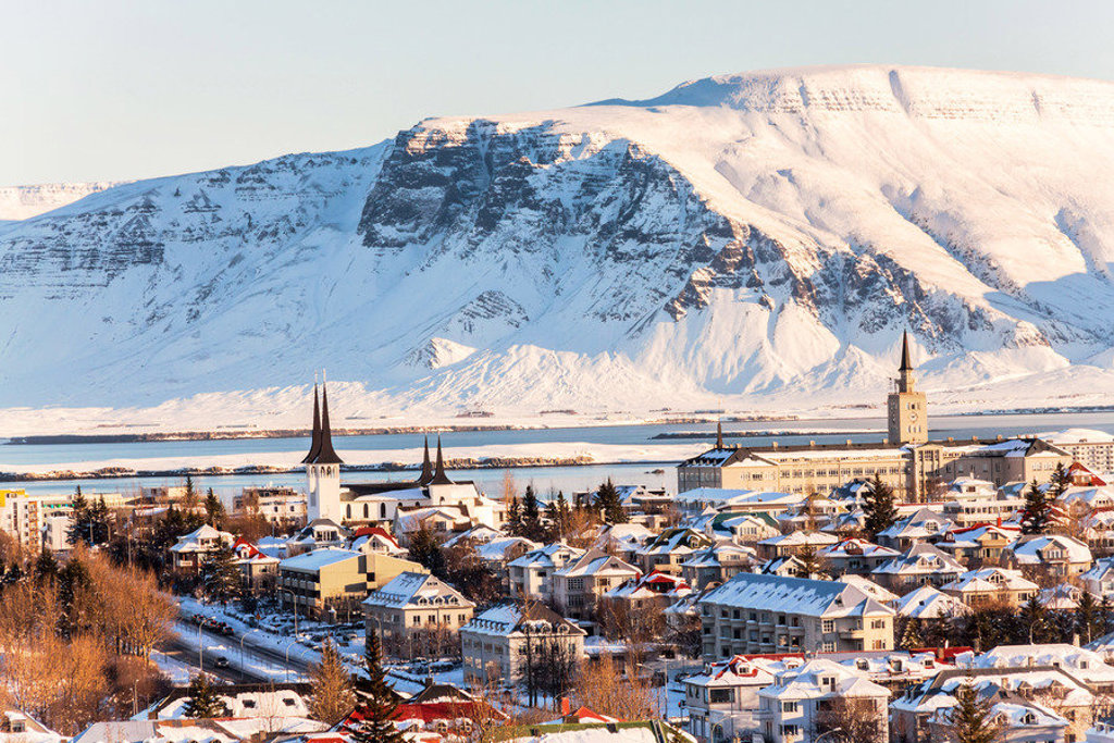 Reykjavik in de winter met besneeuwde huizen en kerktorens, met berglandschap op de achtergrond.