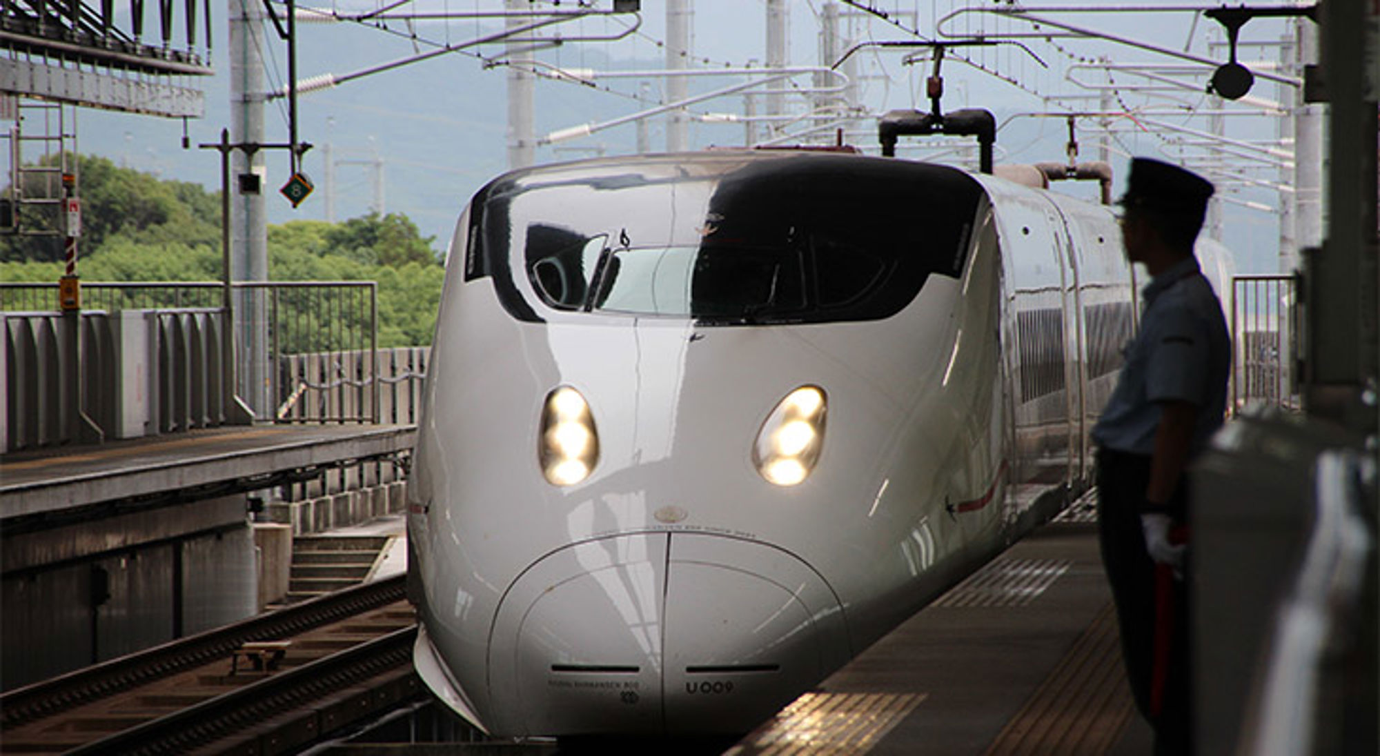 Shinkansen op station Witte hogesnelheidstrein op het perron, met een stationsmedewerker op de voorgrond.