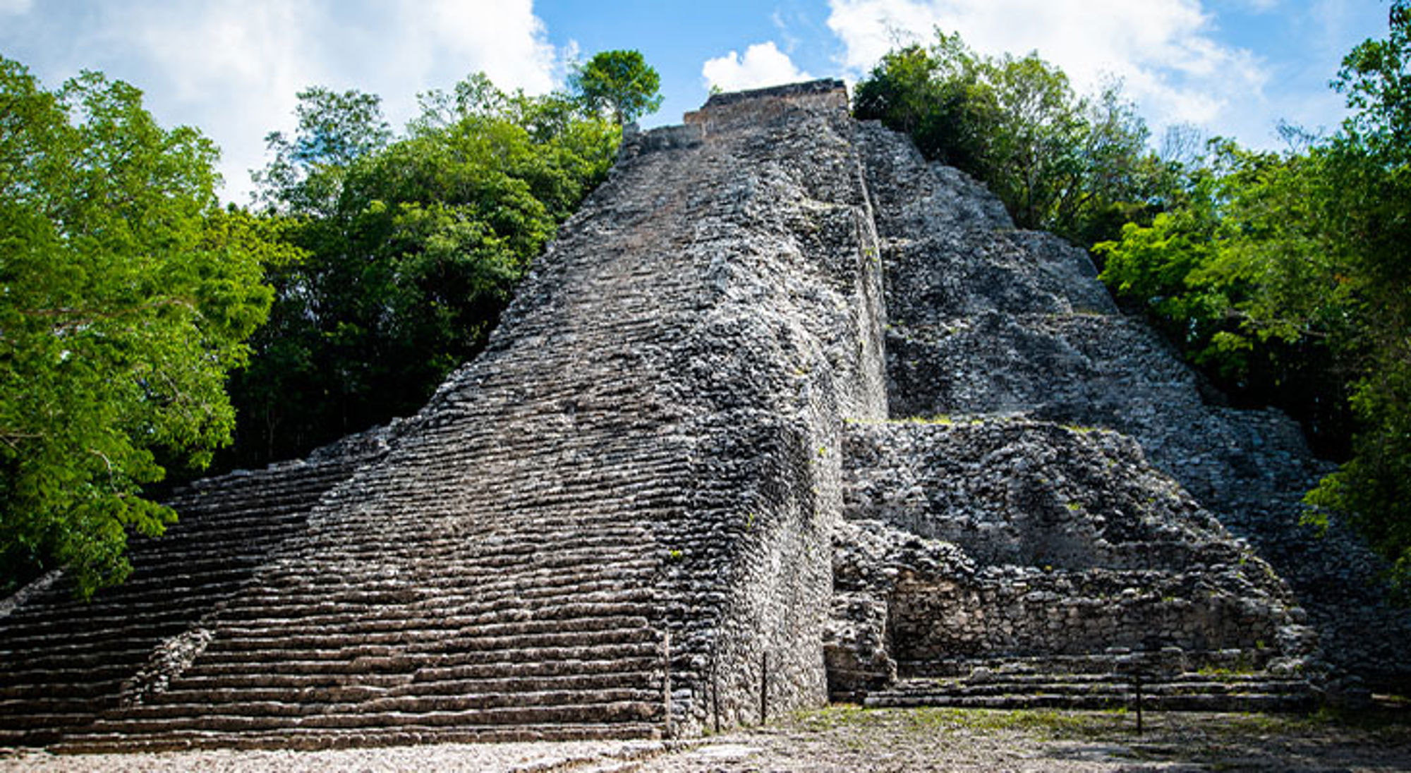 Cobá Steile Mayapiramide met stenen trappen, omringd door jungle onder een blauwe lucht.