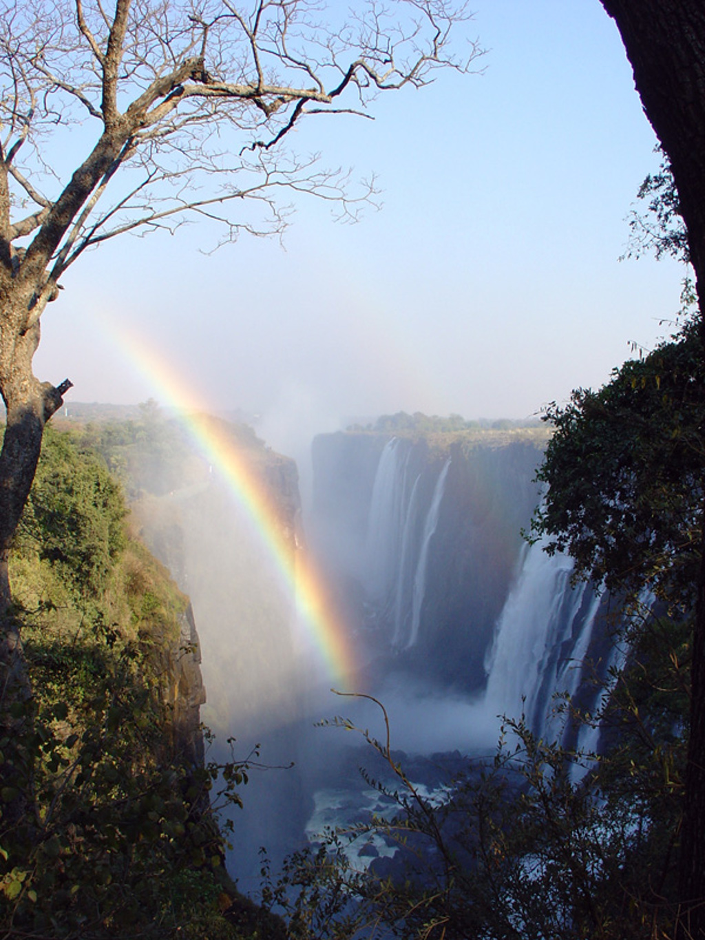 Regenboog boven de Victoria Falls in Zimbabwe, met watervallen die in een diepe kloof storten.