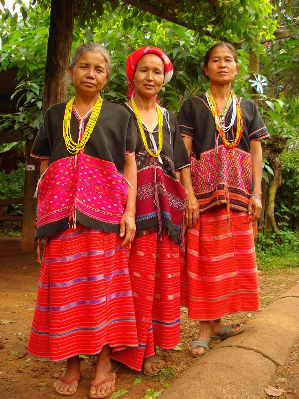 Drie vrouwen in traditionele kleding met kleurrijke rokken en kralenkettingen tijdens een groepsrondreis Thailand.