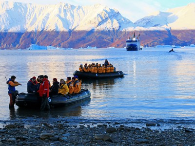 Zodiacboten met reizigers landen aan bij een fjord in Groenland, met ijsbergen en besneeuwde bergen op de achtergrond.