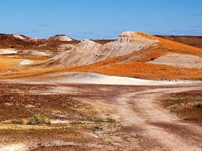 Glooiend woestijnlandschap in Australië met kleurrijke heuvels en een zandpad onder een heldere blauwe lucht.
