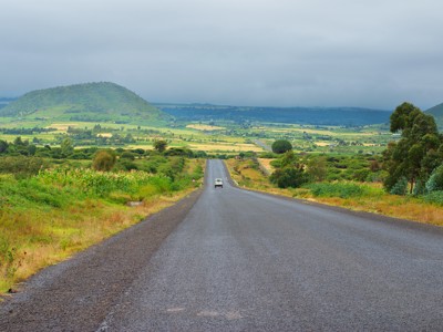 Lange weg door groen heuvellandschap op de route Kenia en Tanzania, met een auto in de verte.