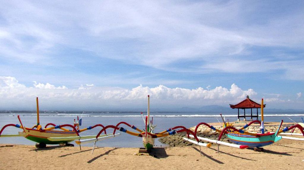 Traditionele vissersboten op het strand van Bali, met een paviljoen aan zee op de achtergrond.