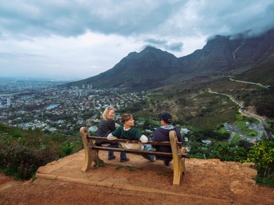 Uitzicht vanaf een bankje over Kaapstad en de Tafelberg, met drie reizigers op de voorgrond.