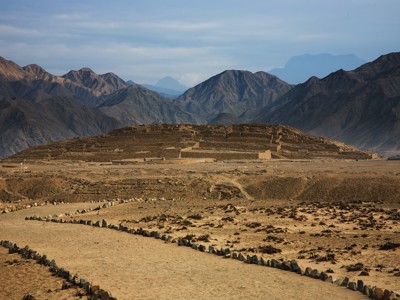 Archeologische ruïnes in een woestijnlandschap met bergen op de achtergrond in Noord-Peru.