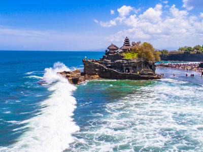Tanah Lot-zeetempel op rots in zee bij Bali, met brekende golven en bezoekers op het strand.