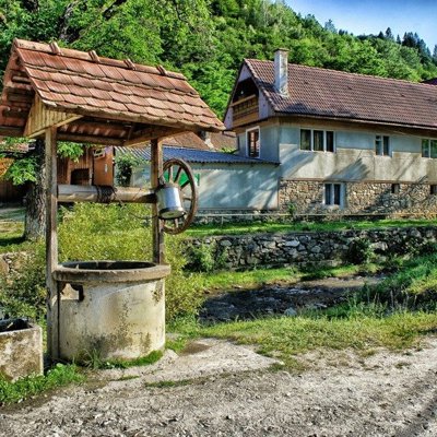 Traditioneel houten huis in Roemenië met steil dak en veranda, omringd door bomen.