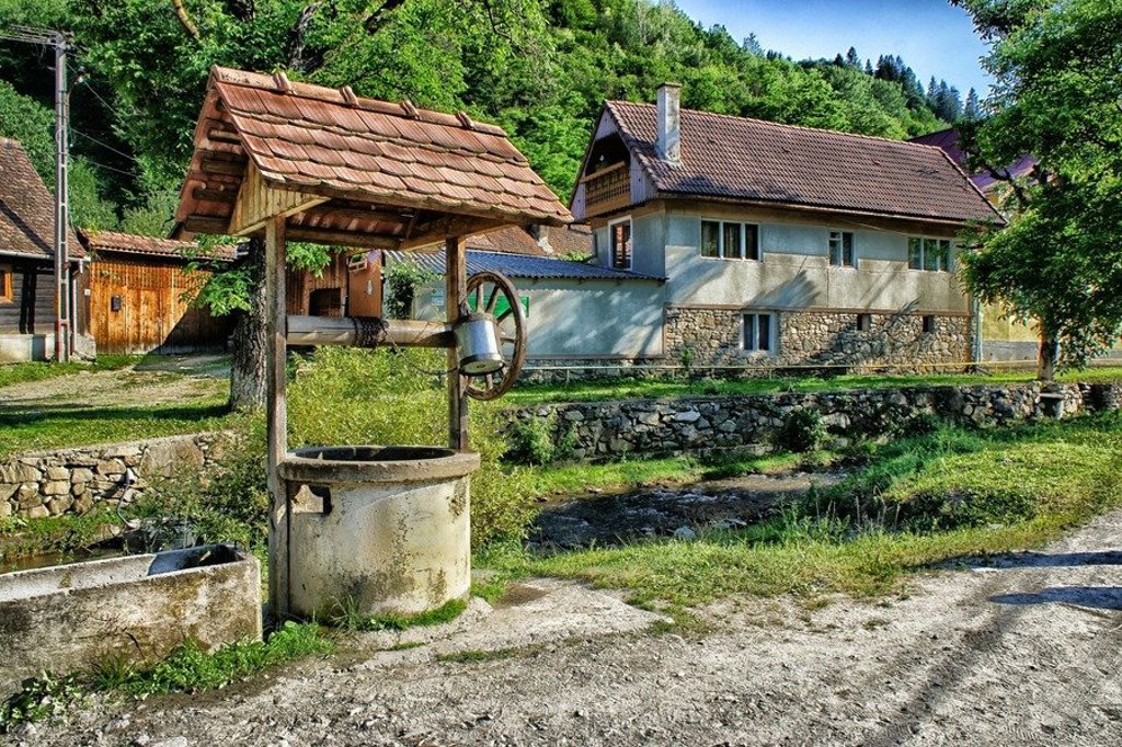 Traditioneel houten huis in Roemenië met steil dak en veranda, omringd door bomen.