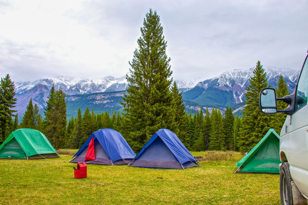 Kampeerplek met tenten in de Canadese Rockies, met besneeuwde bergtoppen en dennenbos op de achtergrond.