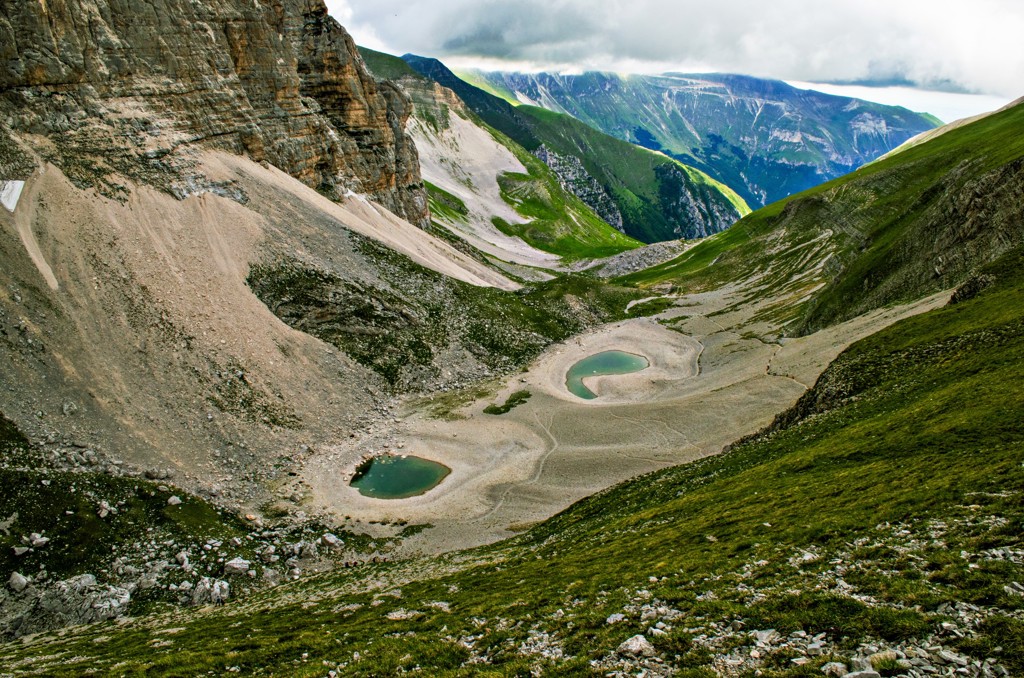 Berglandschap in de Centrale Apennijnen met groen dal, rotswanden en twee bergmeren onder een bewolkte lucht.