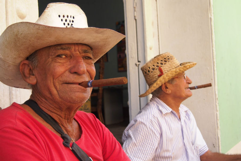 Twee Cubaanse mannen met hoeden roken sigaren bij een deur, tijdens een groepsrondreis Cuba.