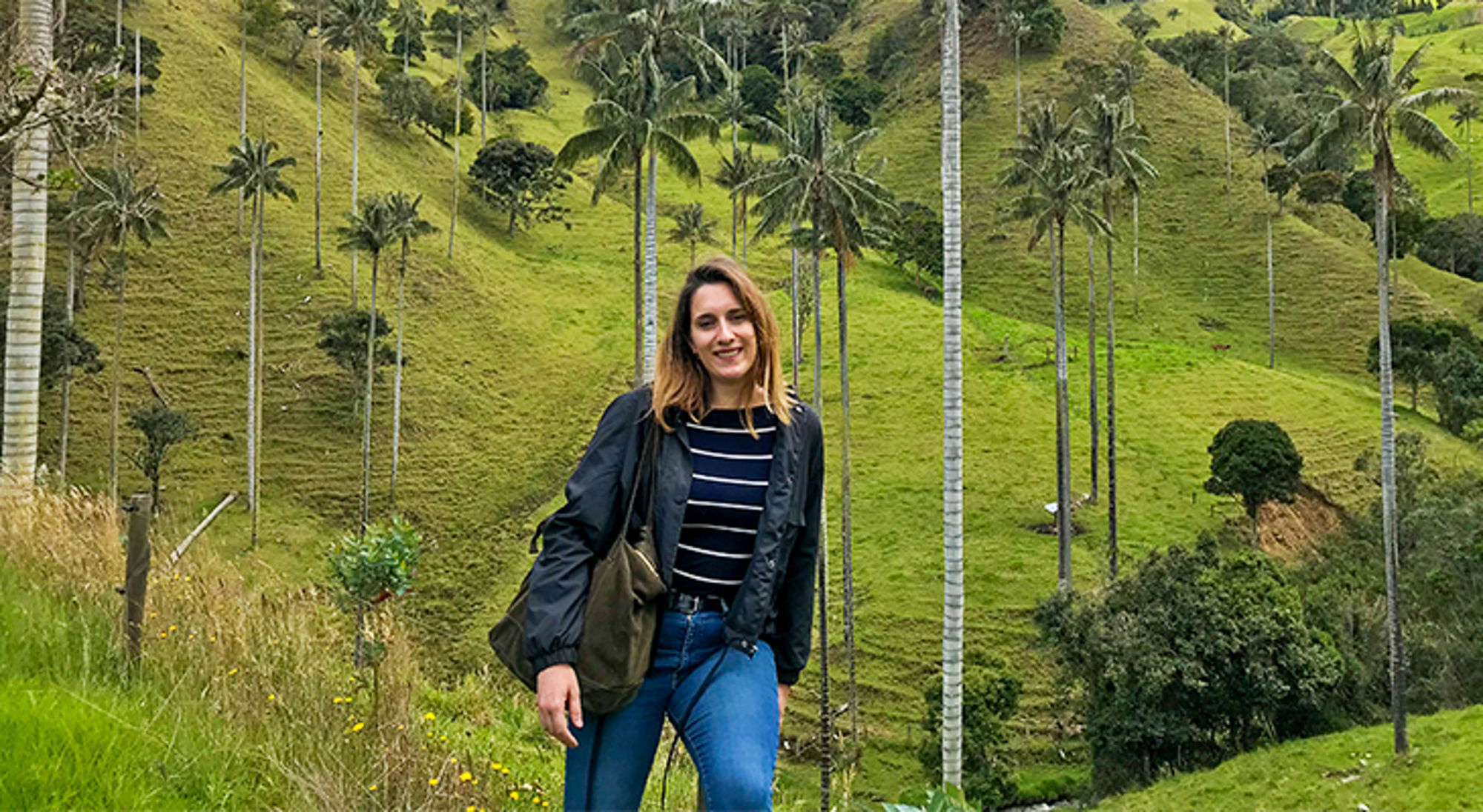 Vrouw poseert tussen hoge palmbomen op groene heuvels in de Cocora-vallei, Colombia.