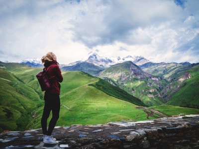 Wandelaar met rugzak kijkt uit over de groene bergen en besneeuwde toppen van de Kaukasus in Georgië.