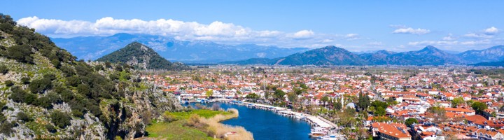 Uitzicht over de Dalyan-rivier met bootjes, rietlanden en het stadje Dalyan tegen de bergen.