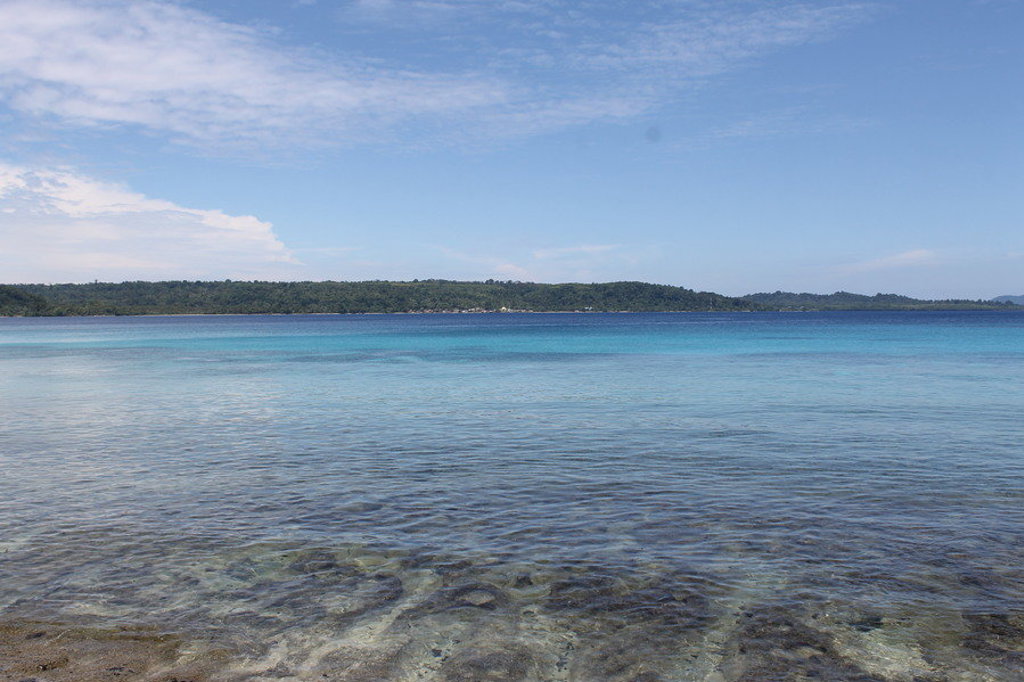 Helderblauwe zee met ondiep water en een groen eiland aan de horizon op de Molukken, Indonesië.
