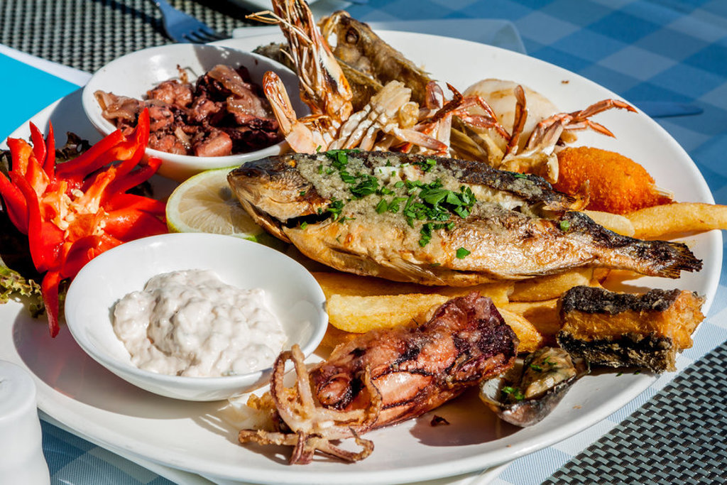Cypriotische visschotel met gegrilde vis, garnalen, calamares, friet en saus op een terras.