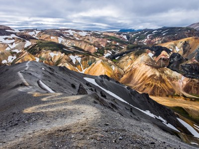 Uitzicht op kleurrijke rhyolietbergen met sneeuwvelden langs de Laugavegur Trail in IJsland.