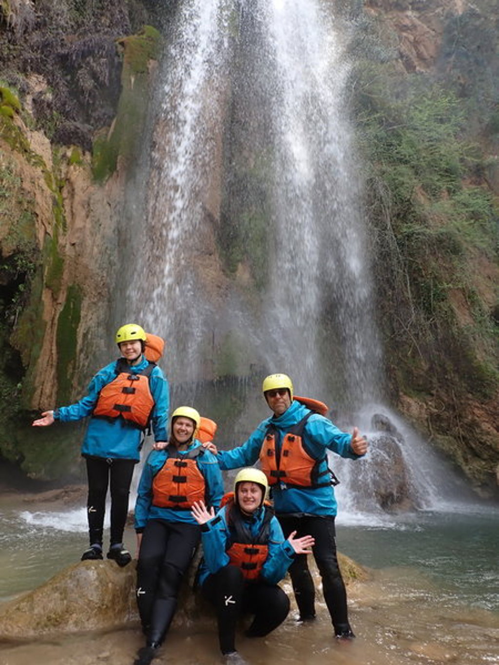 Gezin in wetsuits en helmen bij een waterval tijdens een familiereis in Griekenland.