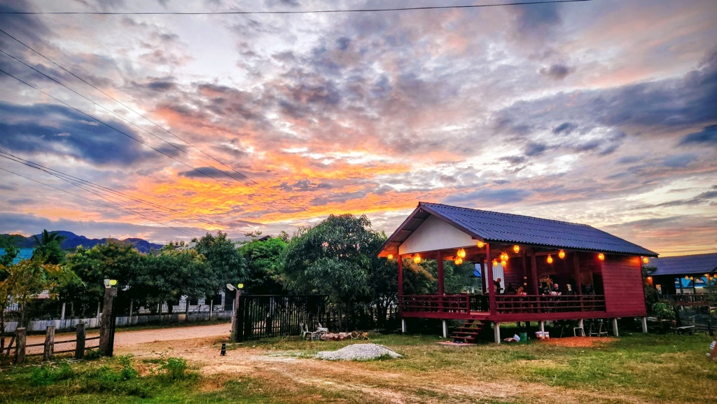 Houten huis op palen met verlichte veranda bij zonsondergang tijdens groepsrondreis Laos & Cambodja.