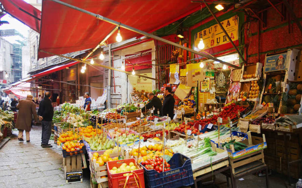 Kleurrijke groente- en fruitmarkt in Zuid-Italië met kramen onder rode luifels.