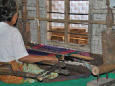 Weefster aan een traditioneel weefgetouw op Lombok, met kleurrijke stof in bewerking.