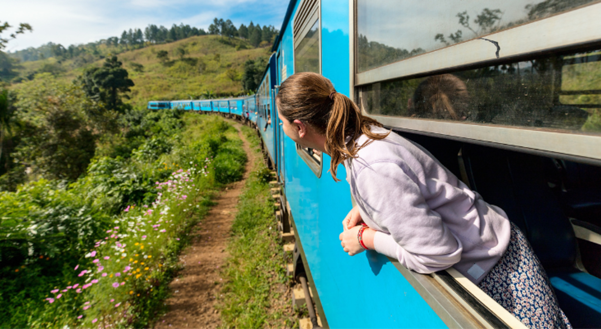 Trein in Sri Lanka Kind kijkt uit het raam van een blauwe trein tijdens een treinreis door groen heuvelachtig landschap.