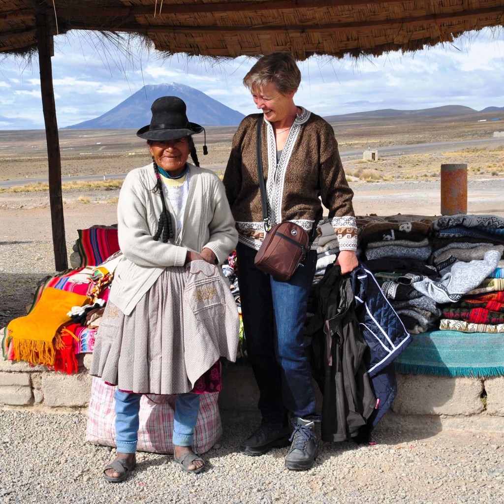 Vrouw op rondreis in Peru ontmoet lokale marktvrouw bij een kraam met kleurrijke dekens in het Andeslandschap.