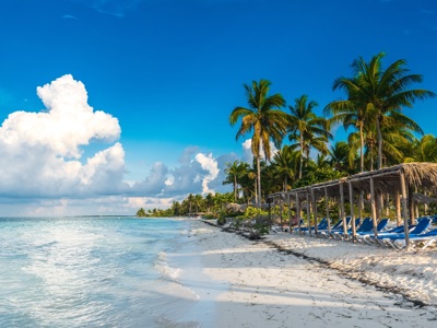 Tropisch strand in Cuba met palmbomen, ligbedden en rieten parasols aan helderblauwe zee.